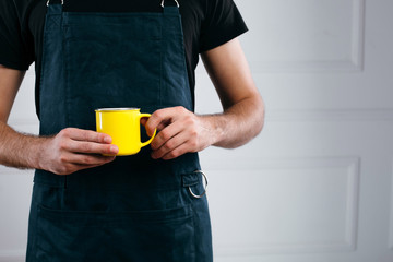 Closeup of barista hands in green apron holding yellow cup of coffe for client