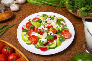 Salad of avocado, tomato, radish, cucumber and mint with yogurt sauce on a brown table. Selected focus.
