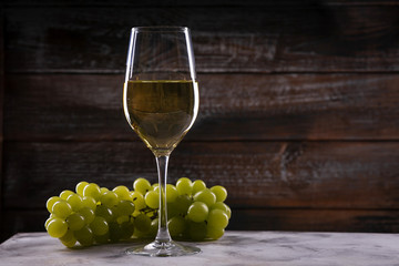 White wine glass with grapes on a table on a wooden background