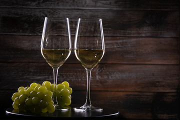 Two full white wine glasses with grapes on a table on a wooden background