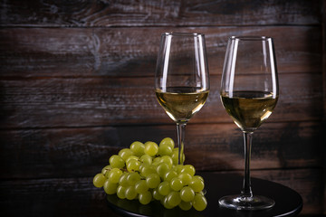 Two full white wine glasses with grapes on a table on a wooden background