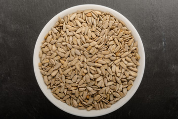 Fresh raw organic sunflower seeds in a white round bowl on a table in soft focus, isolated on black background, top view or flat lay of healthy food