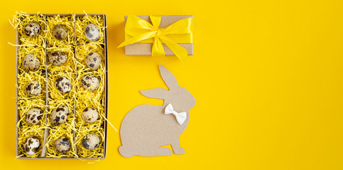 Easter eggs in a paper box. Easter Bunny with a bow.  Easter gift with yellow ribbon. Empty space for a greeting card. Yellow background is creative .top view