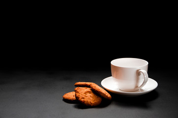 A white cup of coffee with homemade orange biscuits stands on black