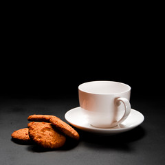 A white cup of coffee with homemade orange biscuits stands on black
