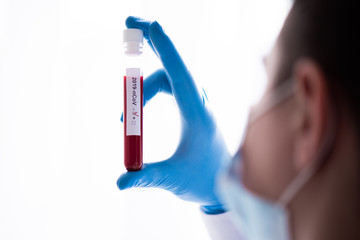 Obraz premium Test tube in male hand close up, doctor in medical mask holding vial with red liquid. Concept blood sample, coronavirus diagnostic, medical research