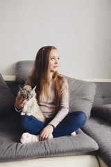 Young trendy woman sitting on the couch at home with domestic cat