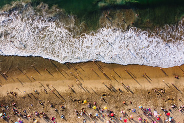 Bird's eye view of crowded beach with bathing people. People relaxing on the beach near ocean unedr umbrellas on sunny day. Aerial view of Playa  Caleta Portales. Valparaiso, Chile.