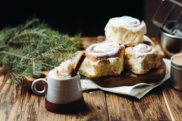 A hot cocoa with cinnamon stick and fresh Christmas buns with powder and over festive table. Winter holidays.