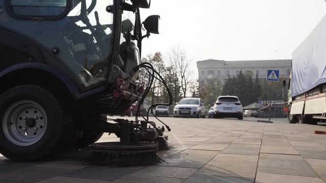 Street sweeper car cleaning city sidewalk paving slabs with pressure washers and rotating brooms outdoors. Road sweeping machine details. Antibacterial sanitary measures on coronavirus quarantine.