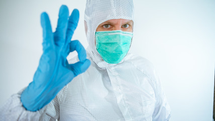 Male caucasian doctor wearing a protective suit and mask making Yes sign gesture