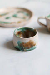 dishes made of white clay covered with green white and brown glaze after firing on a marble light background close-up. pottery top view of a glass, pitcher and plate