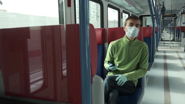 Adult man with medical protective mask and gloves inside empty public transport uses   smartphone then looks around. Disease outbreak, coronavirus covid-19 pandemic, virus protection, quarantine.