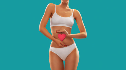 Obraz premium Fit young woman holding a heart over her abdomen, isolated on white background