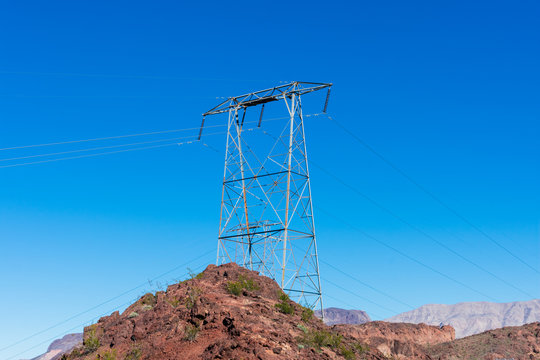 High voltage transmission tower with parallel lines on the top of the rocky hill in the blue sky