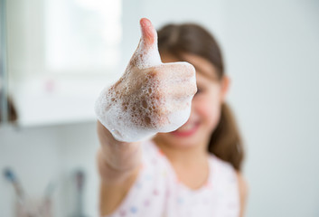 Little girl washing hands with water and soap in bathroom. Kid showing thumbs up. Hands hygiene and...