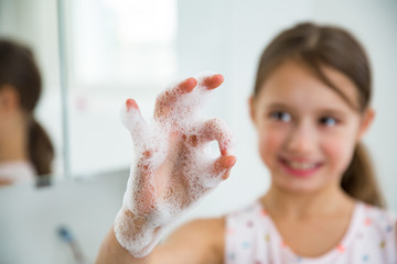 Little girl washing hands with water and soap in bathroom. Kid showing ok sign. Hands hygiene and...