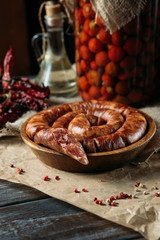 Side view of tasty traditional long sausage in a wooden bowl, dried peppers, spices and oil on the table.