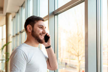 Phone conversation in urban modern office. Smart man negotiating by smartphone.Happy smiling bearded businessman freelancer in cafe.Young caucasian successful man holding smartphone for business work