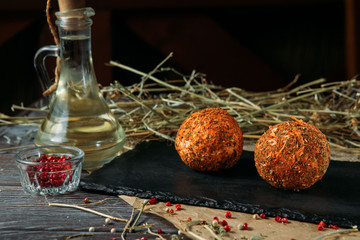 Two mozzarella balls in oil with different spices on a black wooden board on a rustick background.