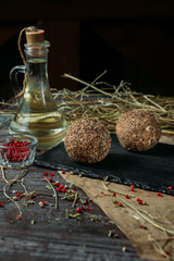 Two mozzarella balls in oil with different spices on a black wooden board on a rustick background.