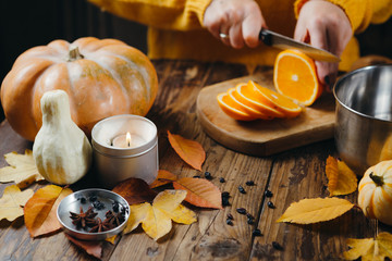 Close-up image of manicured woman's hands cutting oranges on wooden board for hot wine. Pumpkins,...