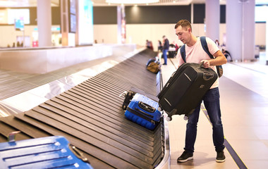 A male European traveler (passenger) picks up his luggage from the  baggage claim tape upon arrival...