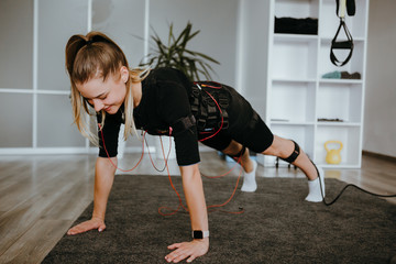 Young woman in EMS training suit with cables doing plank. - obrazy, fototapety, plakaty