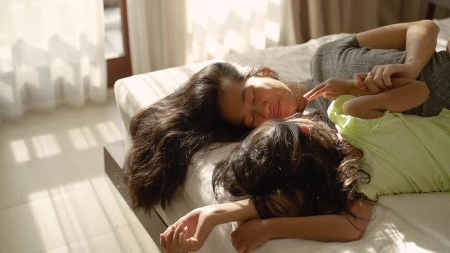 Asian little children lying in bed with their mother next to them in the bedroom