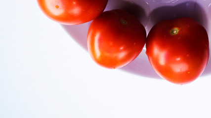 Juicy red tomatoes on a plate with drops of water on a white background. Natural vitamins from vegetables.