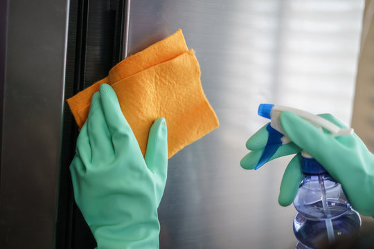 Women hands in rubber green gloves cleaning the Refrigerator at home kitchen,  for corona virus or Covid-19 protection.