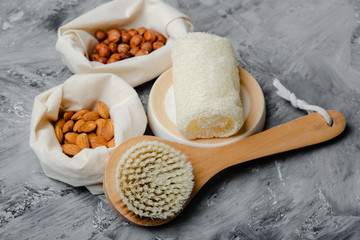 Spa and wellness flat lay on concrete grey background. Body care and cellulite treatment tools, mesh bags with almonds and chestnuts. Natural brush for dry skin peeling or massage and luffa sponge.