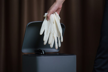 Hand putting used dirty surgical glove to  a garbage bin. Mask protect dust and corona virus in...