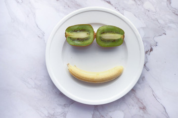 Close up of smile face with kiwi and banana on plate.