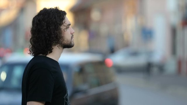 profile of a young man with longer hair puts a mask on his face on the street in the city in slow motion