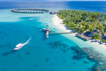 Naklejka na ściany i meble The drone photo with a wooden water villas seen from above and an amazing blue lagoon crystal clear water close to tropical lagoon. Amazing summer travel and vacation background. Dreamy beach scenery