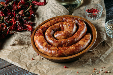 Tasty traditional long sausage in a wooden bowl, dried peppers, spices and oil on the table.