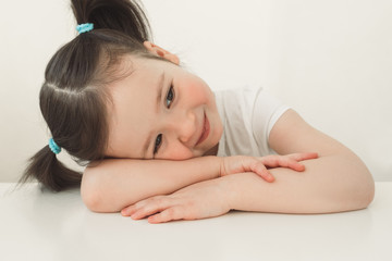 The child sits at the table and smiles sweetly. The girl folded the pens on the table and lies. Cute asian girl