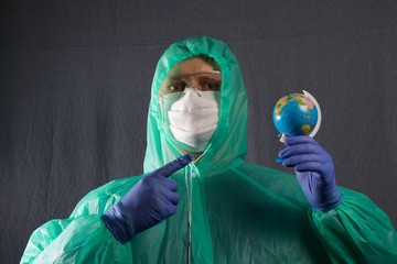 A man in a protective gauze mask, glasses and a raincoat with a hood. Holds a globe in front of him, and points a finger at it. Hands in rubber gloves. Symbol of the global epidemic.