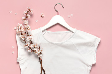 Spring sale concept. White blank women's t-shirt spring twigs of flowers white wooden hangers on pink background flat lay top view. T-Shirt Mock-up. Women's clothes fashion discounts store advertising