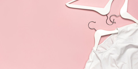 White blank women's t-shirt and white wooden hangers on pink background flat lay top view. T-Shirt Mock-up. Women's T-shirt, clothes, fashion, sale, discounts, store advertising