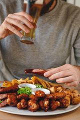 Close-up of man drinking beer, holding sausage. Large hot beer plate with sausages, fries, chicken and sauses on the plate. The concept of dinner.