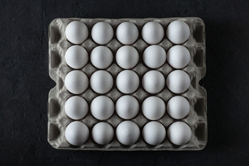 Full cardboard box of white chiken eggs on dark concrete background. Top view. 