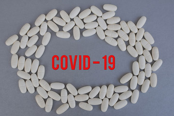 Circle of white medicine tablets or pills on silver color background with red word covid-19 in middle.  Healthcare and coronavirus epidemic concept.