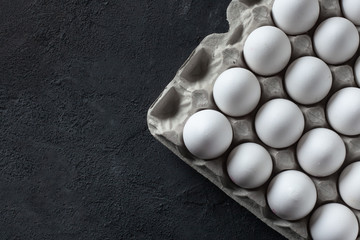 White chicken eggs in a cardboard box on darl concrete background with space. Top view. 