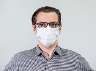 Portrait of an European man in glasses and one-use mask, looking at camera, grey background