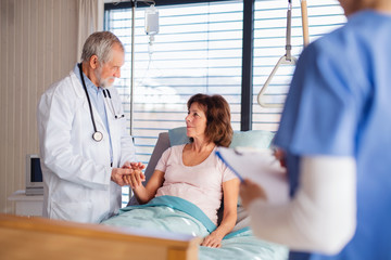 Doctor and nurse examining senior patient in bed in hospital.