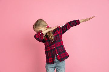 Winner gesture, dabbing. Caucasian little girl's portrait on pink studio background. Beautiful female model with blonde hair. Concept of human emotions, facial expression, sales, ad, youth, childhood.