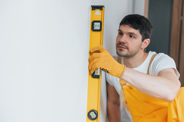 Handyman in yellow uniform checks levels of wall. House renovation conception