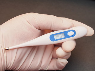 The electronic thermometer is held by a hand in a medical rubber glove. The display shows 39 degrees Celsius.